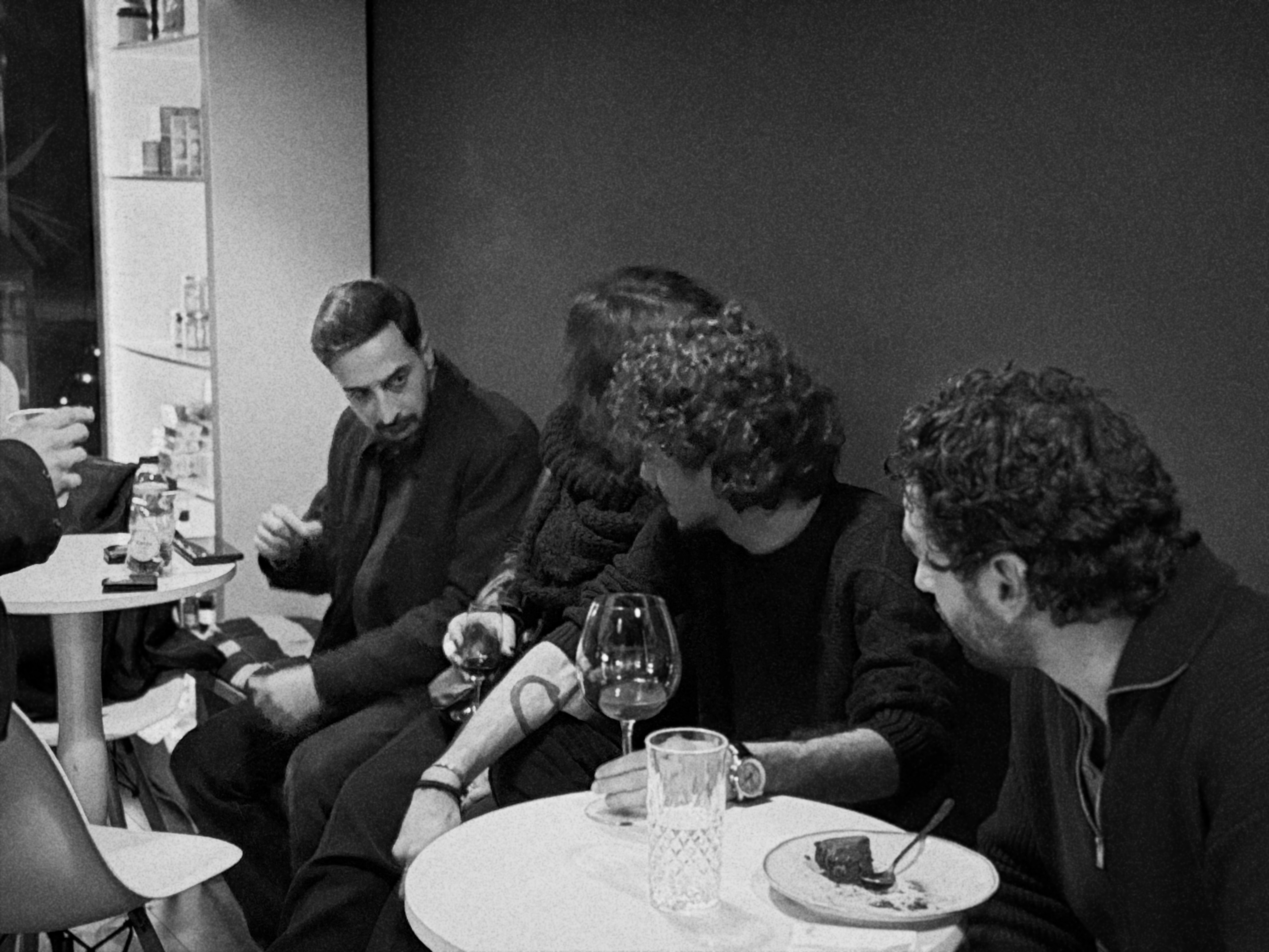 Pessoas sentadas numa mesa de bar em preto e branco, conversando e bebendo.